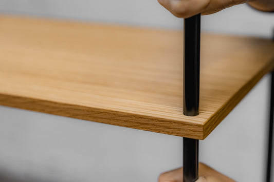 Hands assembling a KUUDU oak board onto the steel rod — tool-free modular furniture